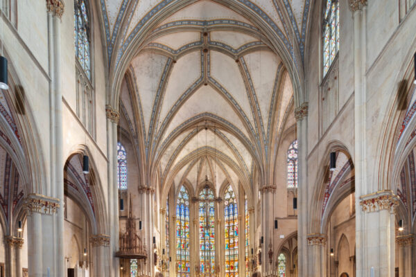 Ganze lange Halle einer Kirche mit hoher Decke vielen Sitzbänken und ausgeschmückten Fenstern