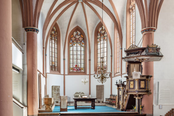 Kirchenschiff mit Bänken und Altar vorne sowie kunstvollen Fenstern