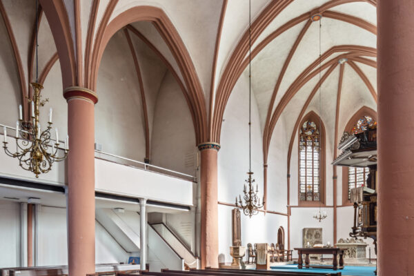 Kirchenschiff mit Bänken im Vordergrund und dem klassischen Kirchestil mit Säulen und Bögen