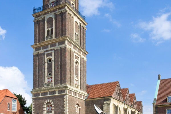 Kirche mit Kirchenturm in Quadratischer Form im Vordergrund mit Uhr und Vorplatz