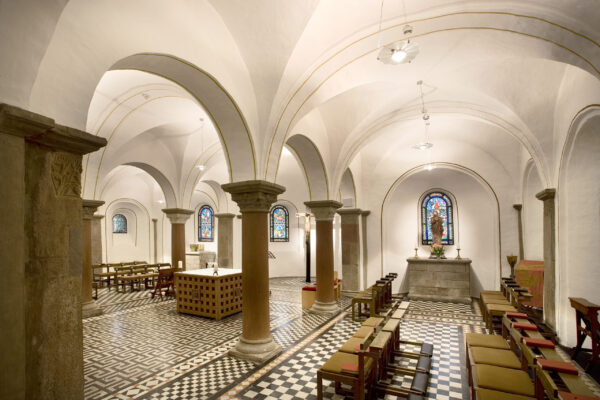 Innenansicht Kirche mit Altar in der Mitte in zwei Richtungen Bänke und in einer Ecke eine Skulptur des heiligen St.Ludgerus
