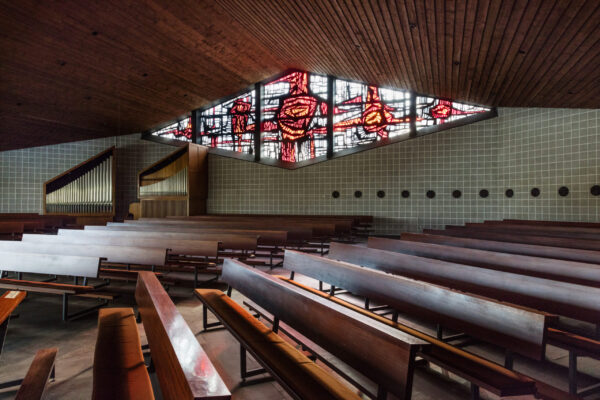 Sitzbänke im Halbkreis mit einer Orgel und einem großen rautenförmigen Fenster