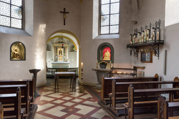 Kapelle mit mehreren Bänken einem Regal mit Kerzen und einem Schrein im Hintergrund